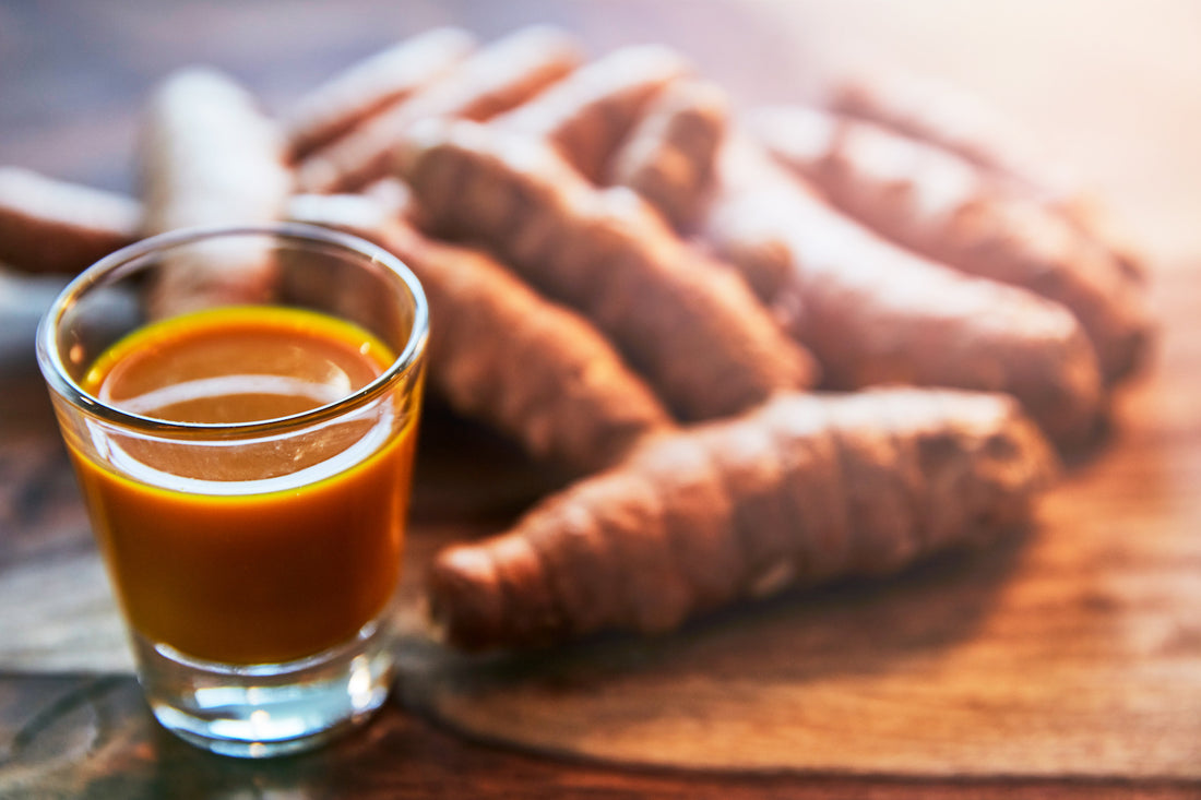 turmeric root and glass of turmeric juice on a wooden chopping board